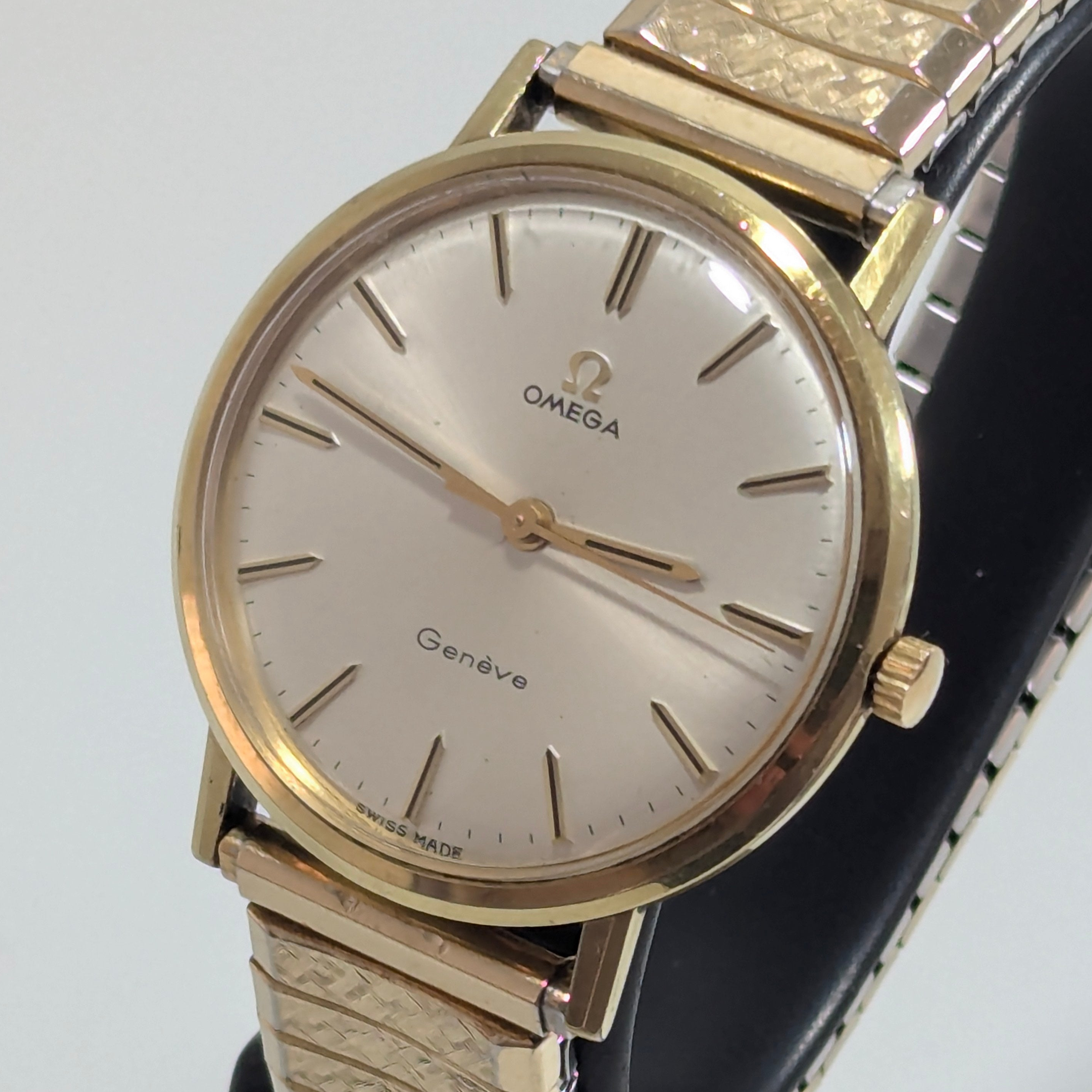 Vintage Omega Genève manual wind dress watch, 36mm gold-tone case, silvered sunburst dial with applied baton indices, gold-tone textured expansion bracelet, three-quarter view