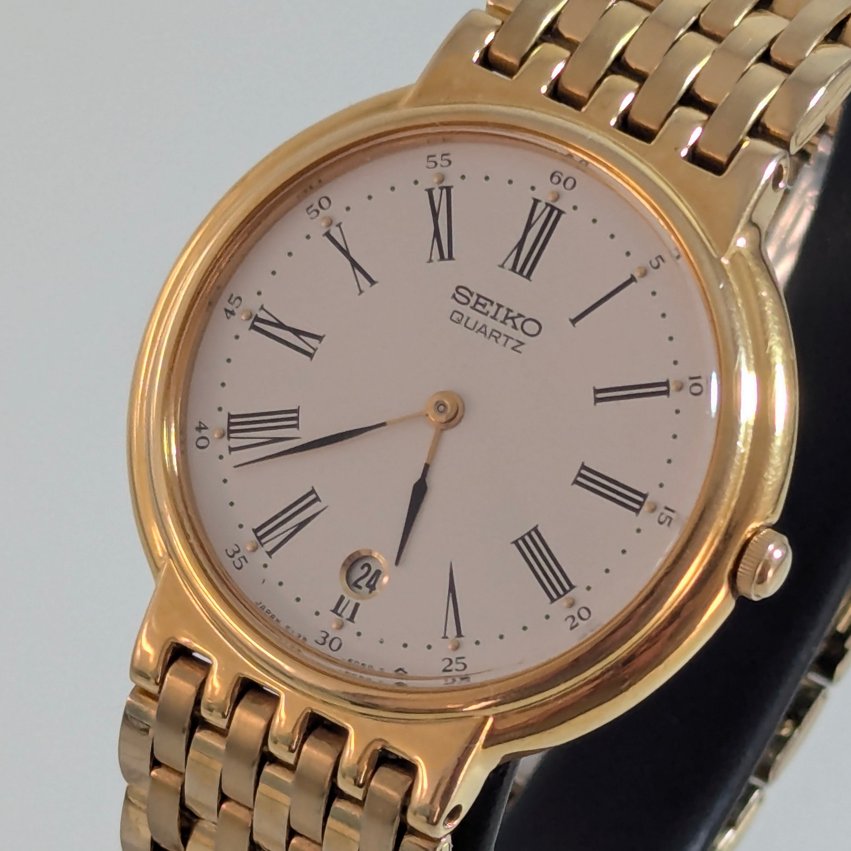 Vintage 1990 Seiko Quartz dress watch, 35mm gold-tone case, white dial with black Roman numerals, date window at 6 o'clock, gold-tone five-row bracelet, front view