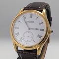 Seiko watch with gold case and brown leather strap on a gray background